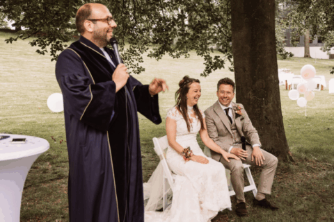 Trouwambtenaar Basti Baroncini spreekt terwijl een bruidspaar naast hem zit